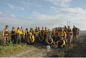 Two dozen people wearing yellow fire gear pose together in a group in an open field at the end of a controlled burn.