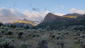 Large mountain peaks at sunrise with sagebrush hills in the foreground.
