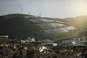 Wind turbines and solar panels on a hill above a town in Portugal in the setting sun