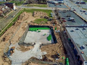 Aerial view of a large underground cistern under construction in an urban area surrounded by parking lots and roads.