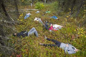 A group of people lie down along a path in a forest.