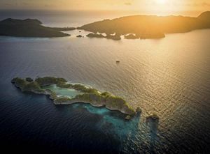 A glowing sunset shines over islands in this aerial view of an island and reef in Raja Ampat.