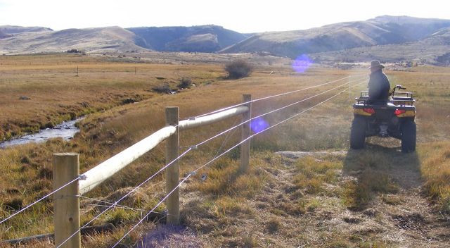 A rancher on an ATV surveys his wildlife-friendly fence. 