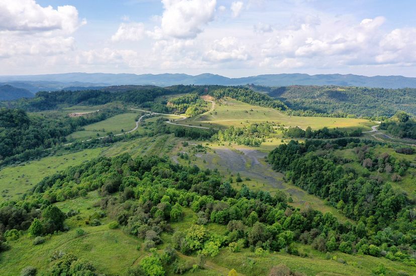 Aerial view of former mine lands in SW Virginia. A dark, bare earth scar lays in the center of an open field that is being reclaimed by grass. The patch is circled by trees and ringed by paved roads.