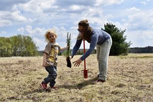 A woman and her son plant a red spruce sapling in a field.