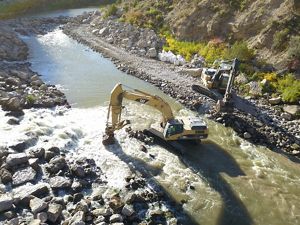 A construction crane removing boulders in a river.