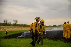 Two fire technicians walking together in front of a grassland that has been burned.