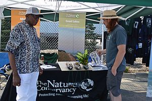 TNC staff speaking with Sacred Heart parishioner in front of a table with a black tablecloth with a white TNC logo on it.
