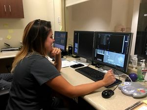 A technician smiles as she sits at a computer monitor.
