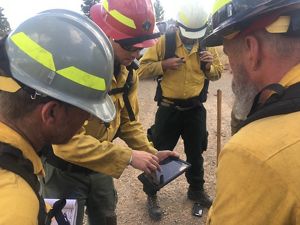Three women work on a chainsaw over a table outside during a TREX fire training session in North Carolina.