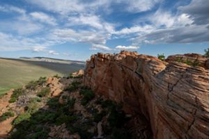 Landscape view of a large red rock wall stretching out into a green landscape.