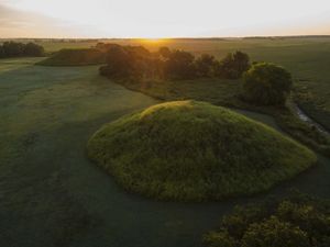 A grass covered mound rises above a flat field in Mississippi.