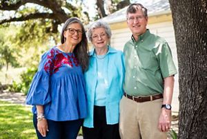 Two women and a man pose together in front of a house.