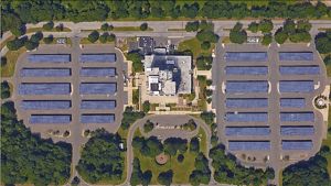 Aerial view of a 5 rows of solar arrays surrounded by trees with a building in the center.