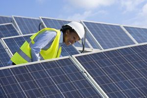 Woman smiles in hard hat while standing in solar panels. 
