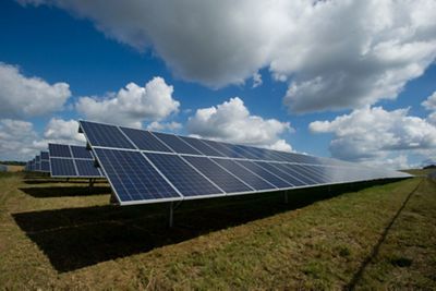 Rows of solar photovoltaic panels spaced apart by grass under a cloudy but sunny sky.