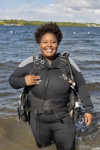 Tiara posing for a photo wearing a wet suit and scuba gear with the ocean behind her.