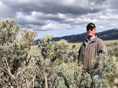 Ken Spackman stands next to a large sagebrush plant in a vast landscape.