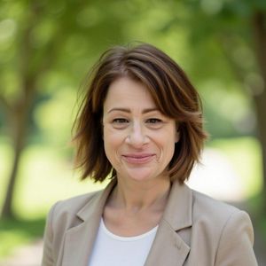 A brunette woman is pictured outside near green trees, smiling for a professional headshot.