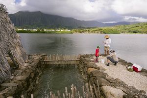 Two adults and a child fish at the edge of a body of water.