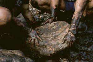 muddy hands move a large stone that will be part of a fishpond wall.