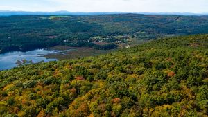 A view of fall trees on a mountain top looking over a river with more mountains in the distance.
