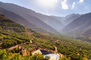 A green farm lies in a valley between dry brown mountain peaks.