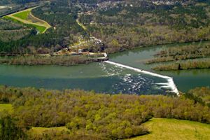 An aerial shot of a dam in a forested landscape with water pouring over the dam. 