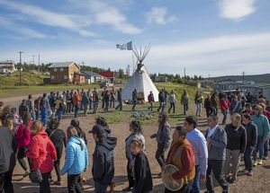 A group of people walking in a circle around a teepee structure.