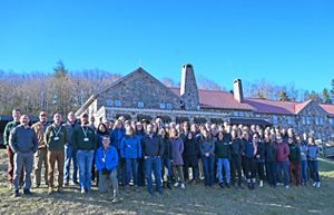 A large group of people stand together outdoors in front of a lodge.