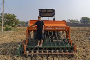 A young woman sits on a farm equipment in wheat field