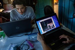 A man works at a computer and a screen shows a camera trap photo of a jaguar.