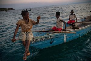 Three children ride on a blue wooden fishing boat.