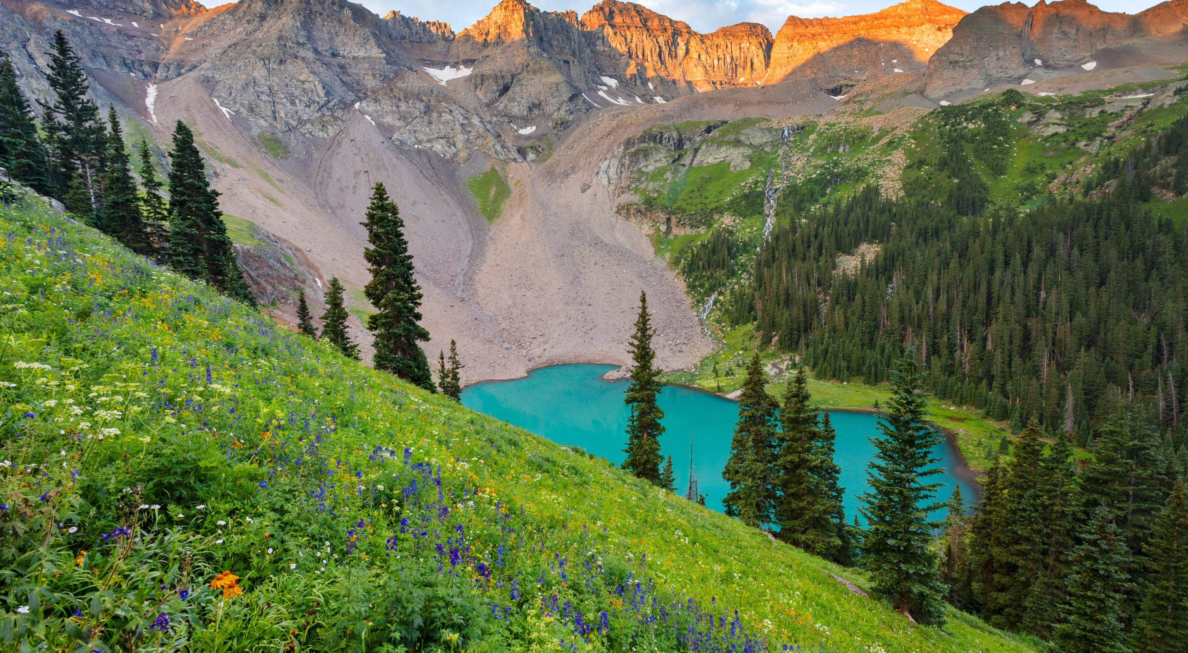 A turquoise lake sits beneath mountains and green grass hills.