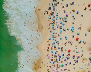 aerial view of beachgoers with colorful umbrellas on a beach on the ocean.