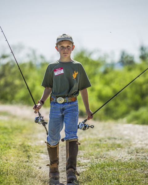 Boy holding a fishing pole in each hand looks at camera