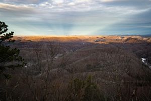 Distant mountain ridges that stretch to the horizon are bathed in golden sunlight. The landscape in the foreground is deep in shadow.