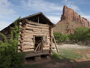 An old ranch building is dwarfed by red rock canyonland.