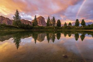 Sunset with rainbow over mountain lake.