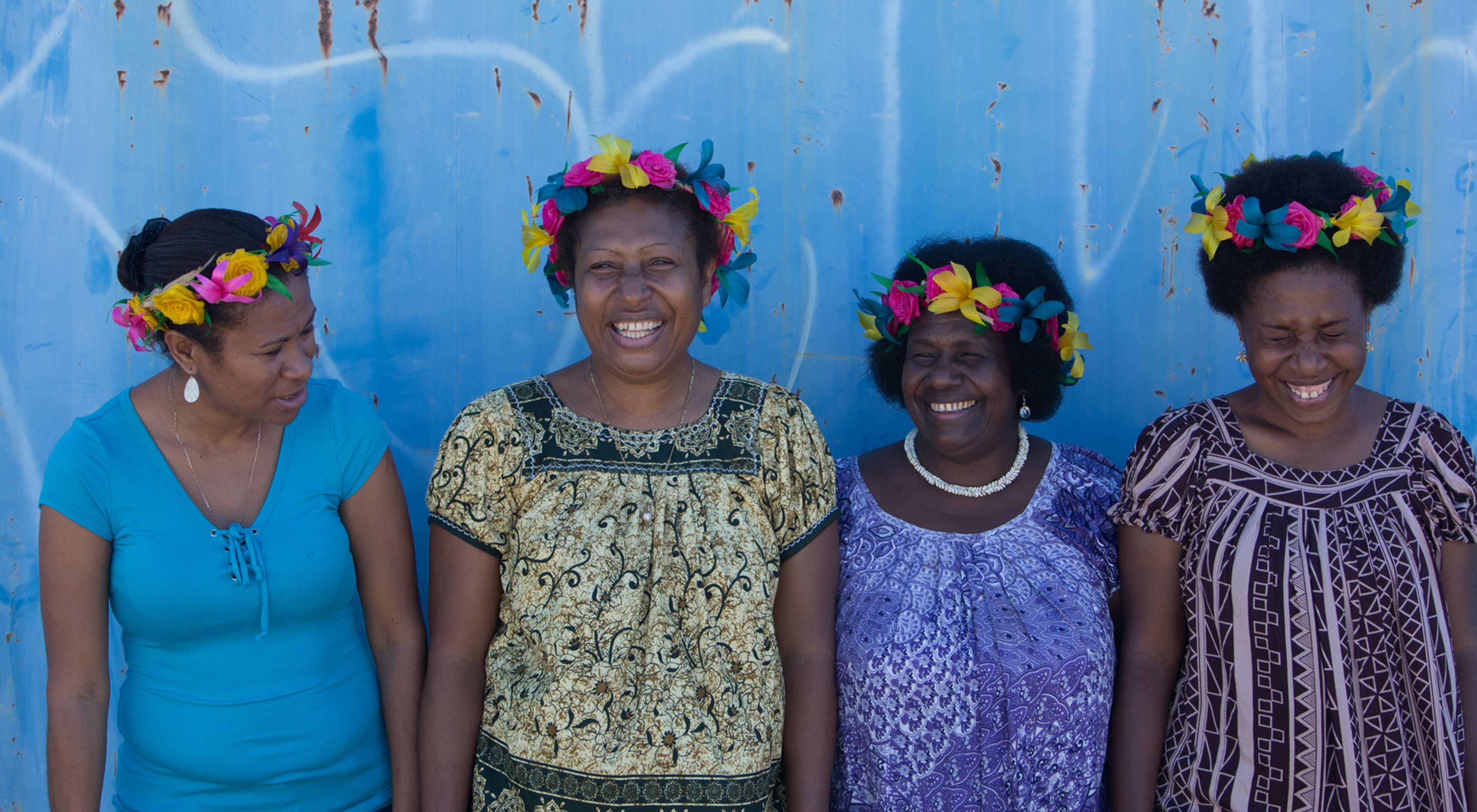 Four Pacific women smiling against a blue background.