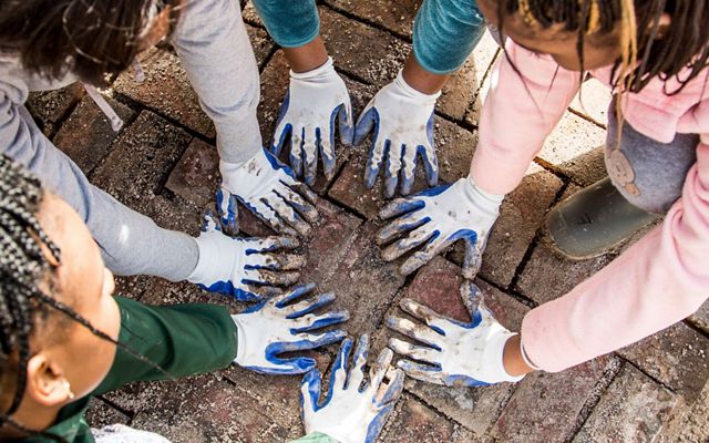 View looking down on four sets of gloved hands placed closely together on a newly laid brick path.