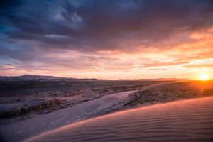 A river running through a landscape of canyons and the sun on the horizon.