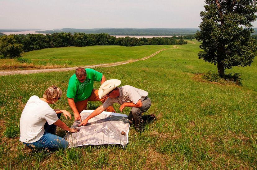 Three people in a field look over a map.