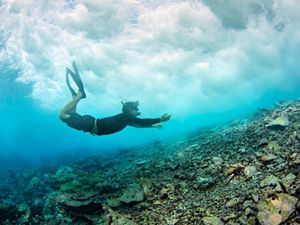 Diver under a breaking wave at the reef crest near Pengiun Spit withing Palmyra Atoll in the equatorial Northern Pacific.