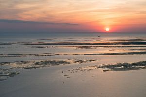 The sun sets over shallow ocean waters.