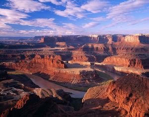 A wide river curves through a landscape of towering mesas that glow red and golden in the sun.