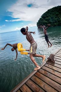 Three people dive off of a wooden dock into the ocean.