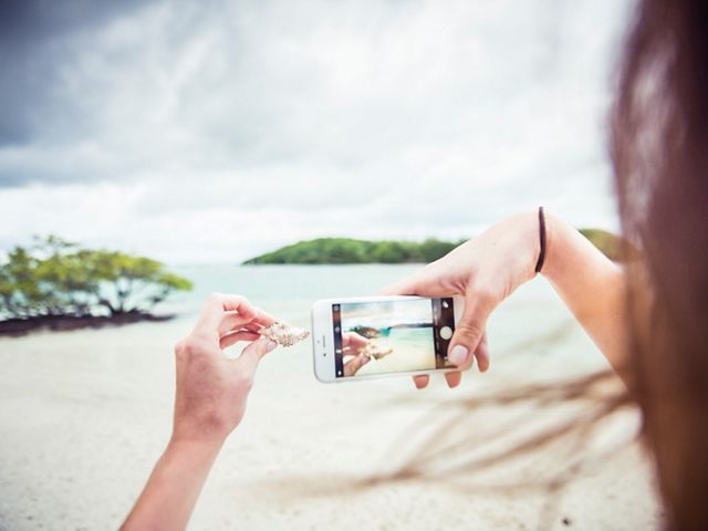 woman uses iPhone to photograph hermit crab shell on a beach