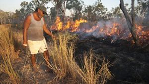 A man standing next to a controlled burn in grass.