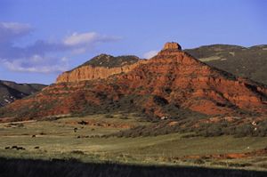 Large red-rock cliffs tower above a rolling green landscape.